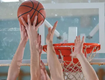 A pair of hands looking to dunk a basketball with other pairs of hands looking to block them.