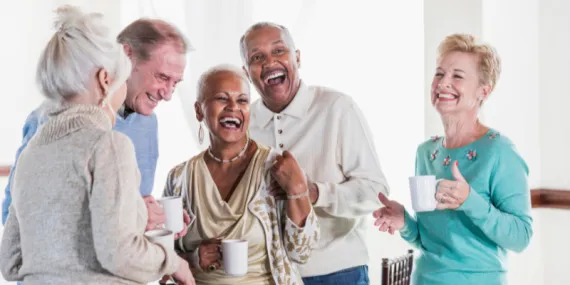 A group of older people smiling and sharing coffee together.