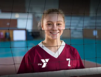Child smiling behind a volleyball net.